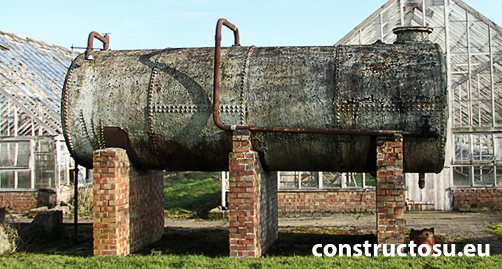 Rezervor de apă din oțel nituit, amplasat lângă o seră.